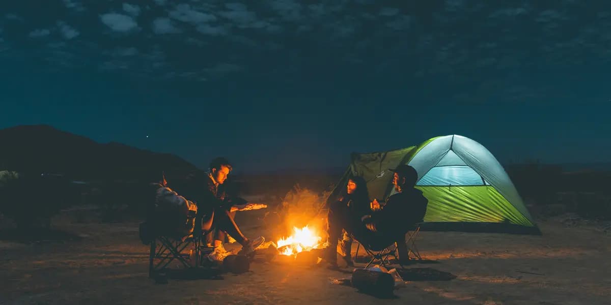 Friends camping at night around a campfire beside a glowing tent
